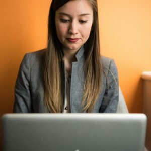 Focused businesswoman using a laptop indoors with an orange background.