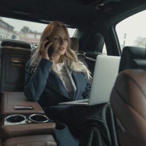 Confident businesswoman making a call and working on a laptop in a luxury car interior.